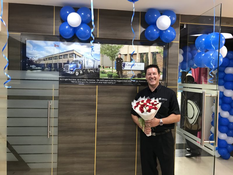 President Brian Bendig posing in front of a picture of Cavalier Tool Canada in the offices of Cavalier Tool India.