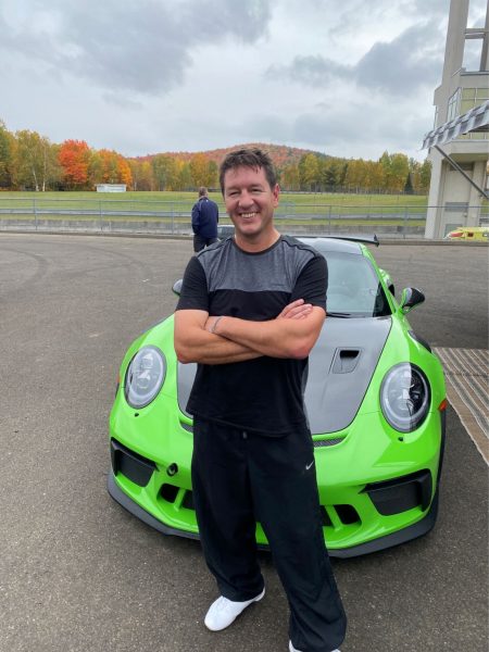 Brian Bendig is an avid racer, he is pictured here in front of his lime green Porsche at a race track.